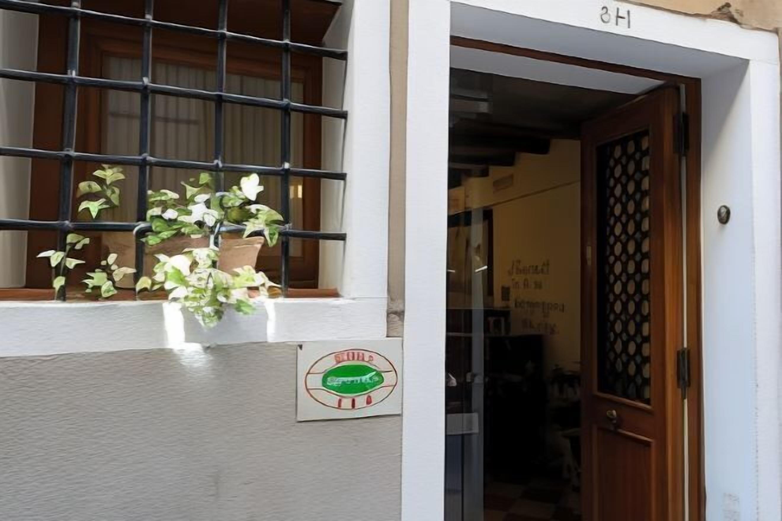 A building entrance with a potted plant on the ledge, a door with a decorative grille, and a sign with a logo.