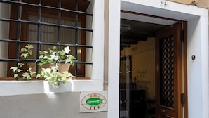 Una entrada de edificio con una planta en maceta en el bordejo, una puerta con celosía decorativa y un letrero con un logotipo.