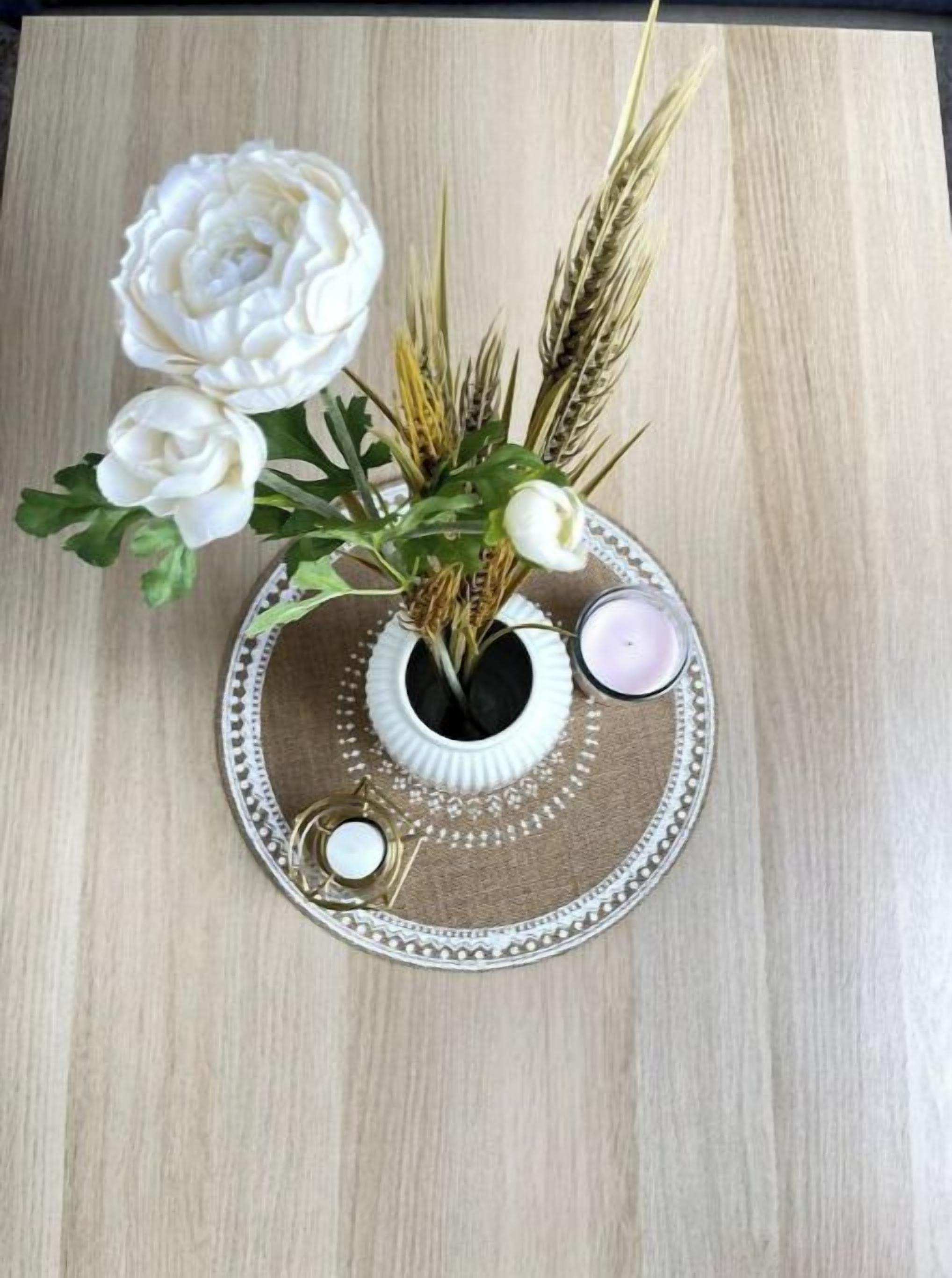 Un vase décoratif orné de fleurs blanches et de tiges de blé, posé sur un tapis texturé.