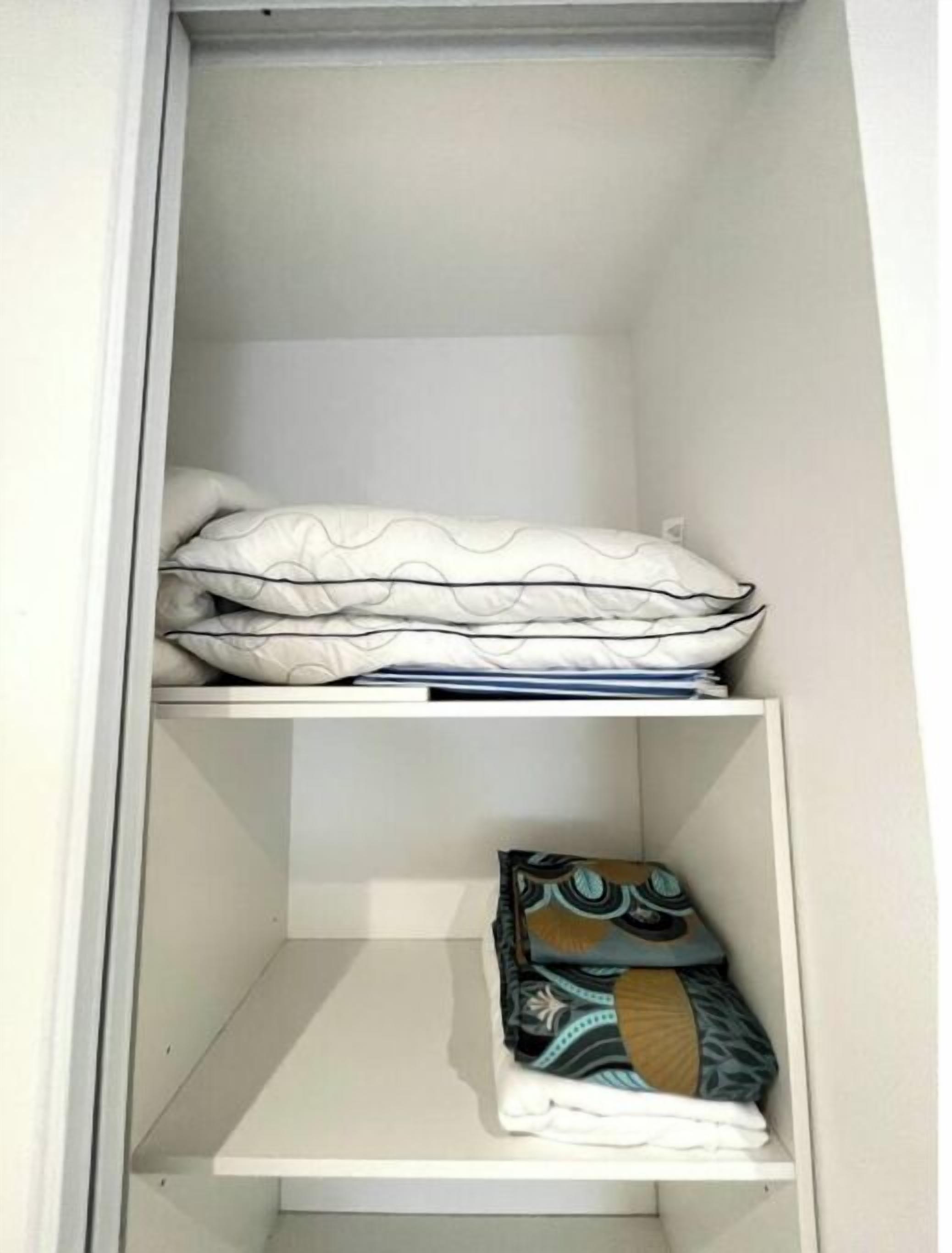Un armario con dos estantes; la parte superior contiene ropa de cama doblada y la inferior, prendas de vestir dobladas.