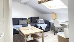 Un appartement moderne de style « loft », doté d’une lucarne, d’un canapé gris foncé, d’une table basse en bois, d’un bureau blanc et d’une chaise blanche.