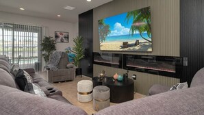 Un salon moderne doté d’un grand téléviseur à écran plat fixé au mur, d’un canapé gris, d’une table basse et d’une cheminée.
