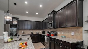 Une cuisine moderne avec des meubles de couleur sombre, des plans de travail en granit, des appareils électroménagers en acier inoxydable et des luminaires suspendus.