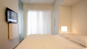 A hotel room with a bed, a television mounted on the wall, a window with curtains, and a small bedside table. - Apartment in Knokke Near Driehoeksplein (Knokke-Heist)