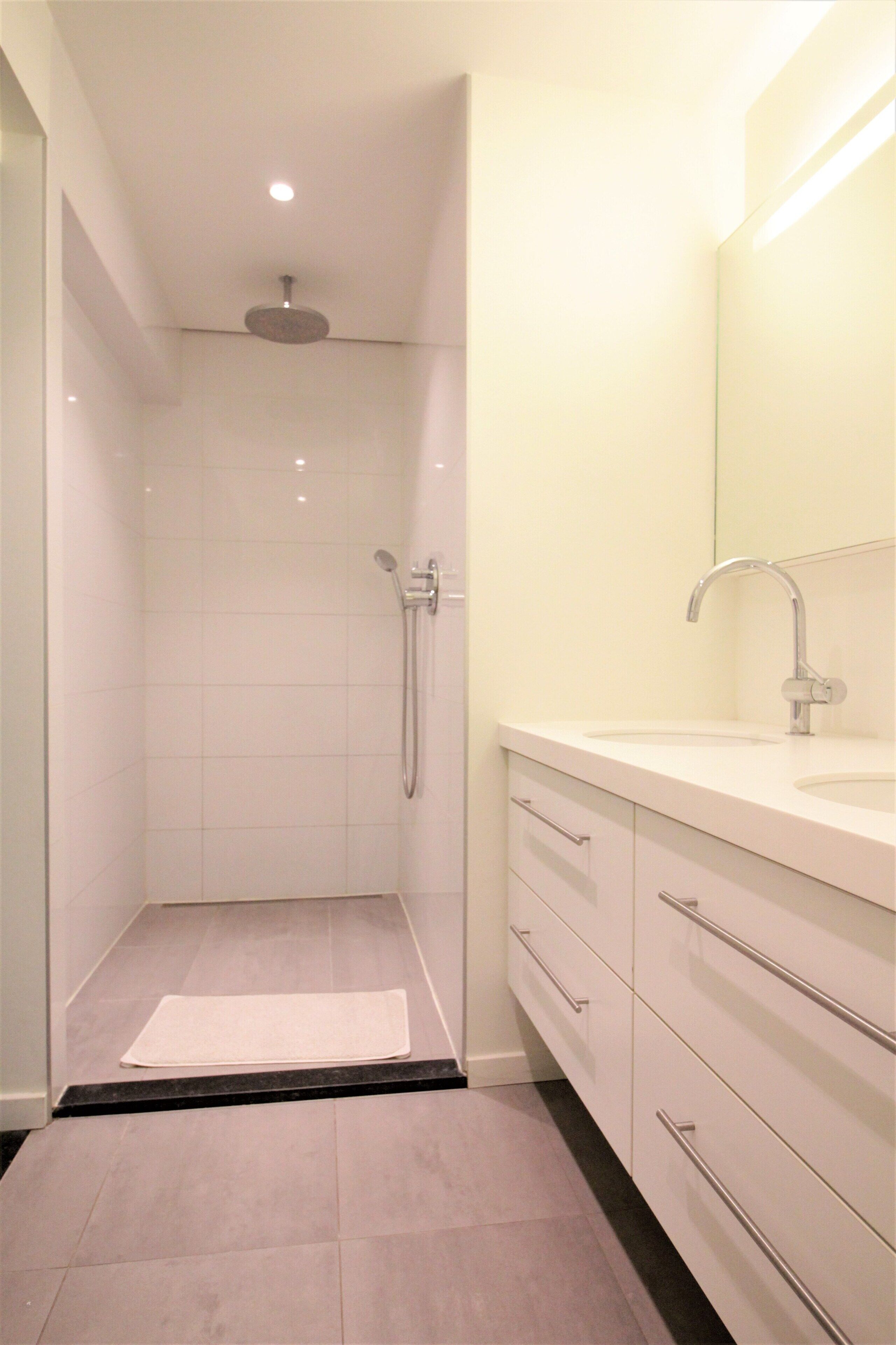 A modern bathroom with a walk-in shower, a sink with a mirror, and a tiled floor.