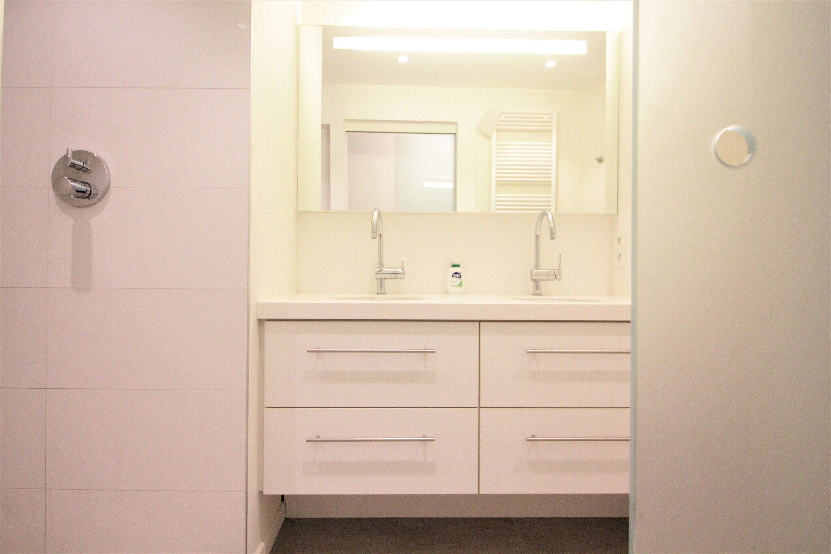 A modern bathroom with two sinks, a large mirror, and white cabinetry.