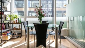 Un'area pranzo moderna con un tavolo in vetro e sedie, un vaso di fiori e una libreria con diversi oggetti.
