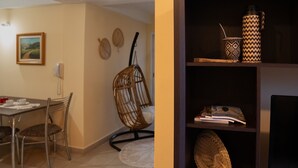 Un comedor con una mesa, sillas y una silla colgante. Se observa una estantería con revistas y objetos decorativos.