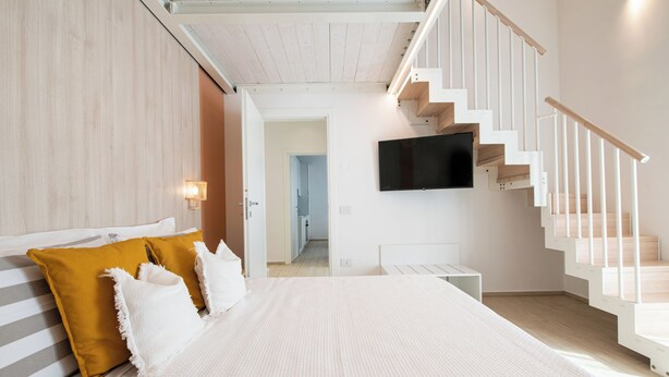 Un dormitorio moderno con una cama grande, una escalera y un televisor de pantalla plana montado en la pared.