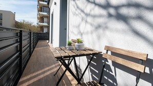 Un balcón con una mesa de madera, dos plantas en macetas y un banco.