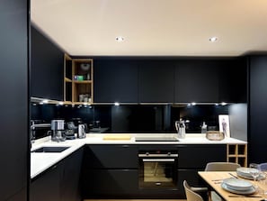 Cozinha moderna com armários pretos, bancada branca e forno embutido.