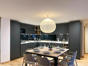 Cozinha moderna com armários escuros, uma ilha central e um espaço de jantar com mesa redonda e cadeiras.