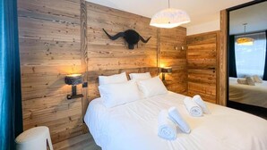 A hotel room with a wooden wall, a large bed with white linens, two bedside lamps, and a mounted animal head decoration.