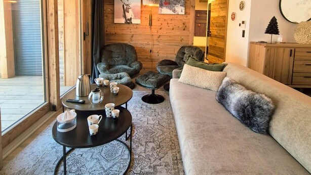 A cozy living room with a large window, a round coffee table, a sofa, and a unique ceiling light fixture.