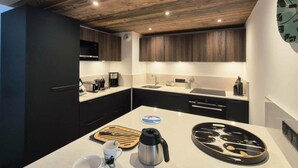 A modern kitchen with dark cabinets, a white countertop, a kettle, a cutting board, and a coffee maker.