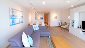 A modern living room with a sectional sofa, a dining area, and a kitchen in the background.