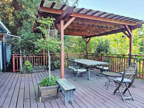 A wooden deck with a pergola, outdoor furniture, and potted plants.