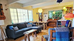 Una sala de estar acogedora con un sofá, una mesa de centro y sillas de madera. Se ve un piano y una mesa de comedor con sillas.
