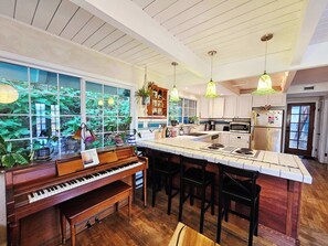 A spacious kitchen with a piano, large windows, and a central island.