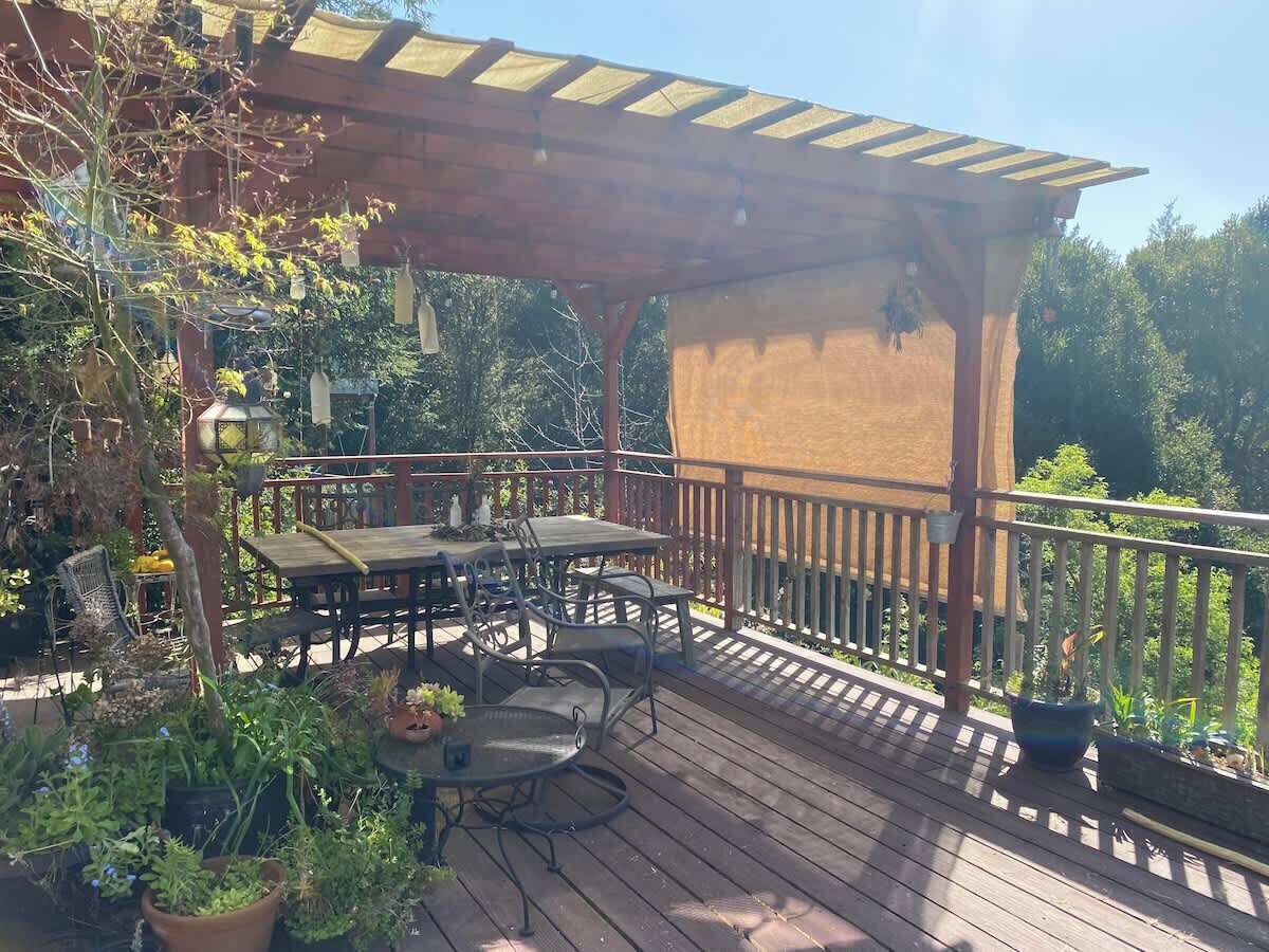 Een houten terras met een pergola, tuinmeubilair en potplanten.
