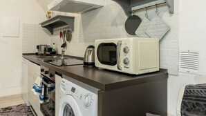 A compact kitchen with a washing machine, a microwave, and a kettle.