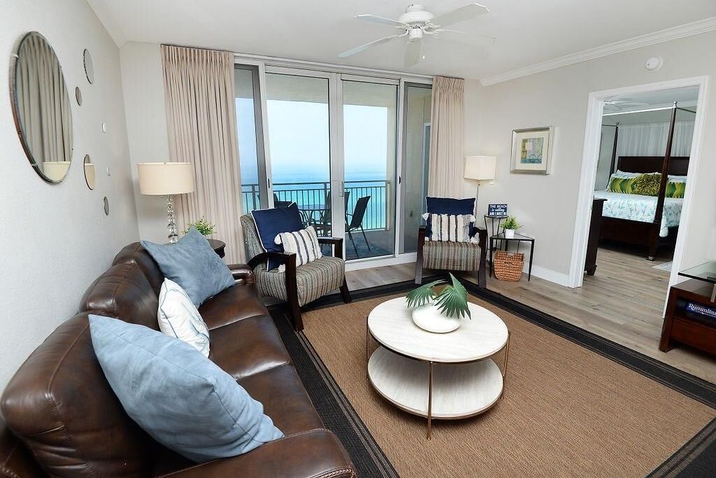 Ein modernes Hotelzimmer mit einem braunen Ledersofa, zwei Sesseln, einem runden Couchtisch und einem Balkon mit Meerblick.