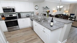 A modern kitchen with white cabinets, stainless steel appliances, and a granite countertop. - Emerald Beach 1130 (Panama City Beach)