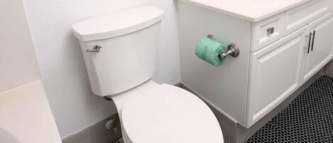 Un baño con inodoro blanco, lavamanos con espejo y un cuadro de una playa en la pared.