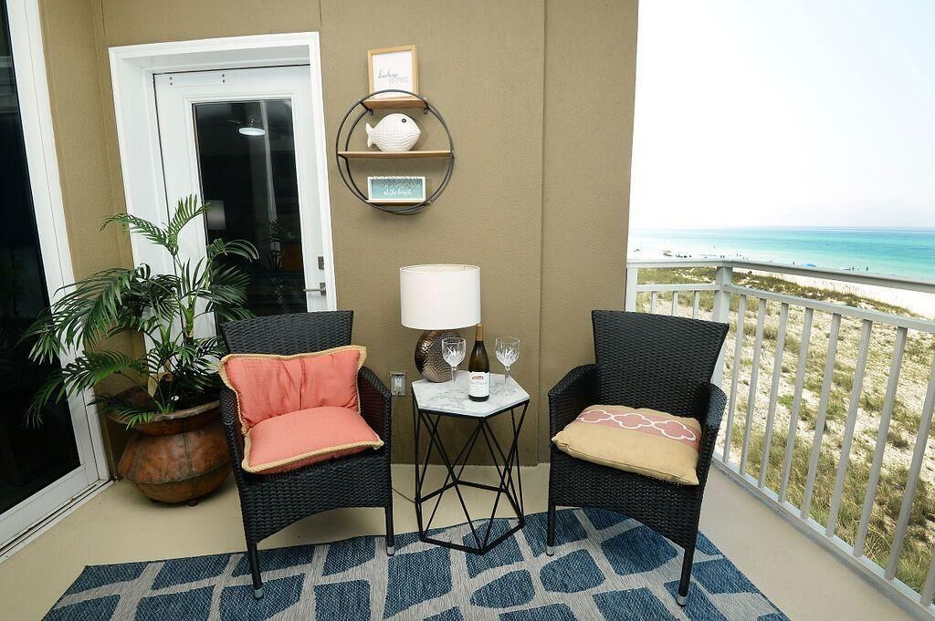 Ein Balkon mit zwei Korbstühlen, einem kleinen Tisch mit Lampe, einem Blumentopf und Blick auf den Strand.