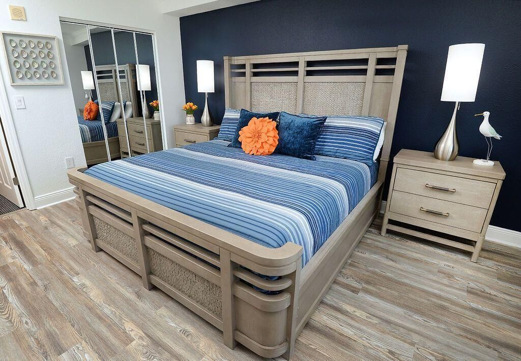 A bedroom with a large bed, a nightstand, a dresser, and a mirror.