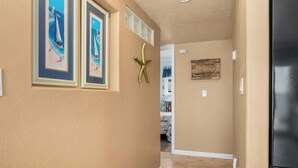 A hallway with beige walls, framed artwork, a decorative starfish, and a black refrigerator.