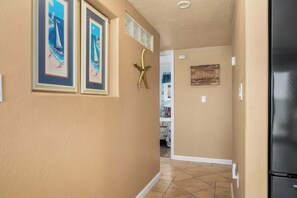 A hallway with beige walls, framed artwork, a decorative starfish, and a black refrigerator. - Rio del Mar Paradise with sweeping oceanviews! (Aptos)