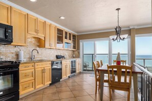 A kitchen with wooden cabinets, a dishwasher, a stove, and a dining area with a view of the ocean. - Rio del Mar Paradise with sweeping oceanviews! (Aptos)