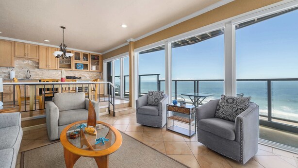 A spacious living area with a balcony overlooking the ocean, a kitchen with wooden cabinets, and a dining area with a glass table.