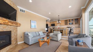 A living room with a fireplace, sofas, a coffee table, and a kitchen in the background.