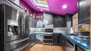 A modern kitchen with stainless steel appliances, a wooden floor, and a purple accent wall.