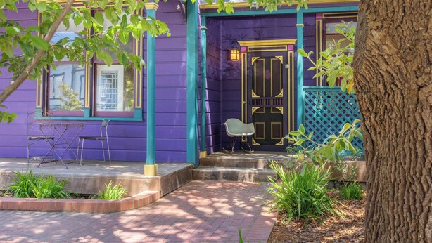 A purple house with a black door, a small porch, and a tree in the foreground.