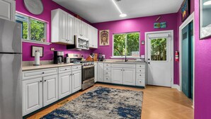 A kitchen with white cabinets, a blue rug, and a purple wall.