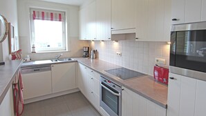 A modern kitchen with white cabinetry, a stainless steel oven, a red toaster, and a window with striped curtains. - Duplex in Knokke Near North Sea Beach (Knokke-Heist)