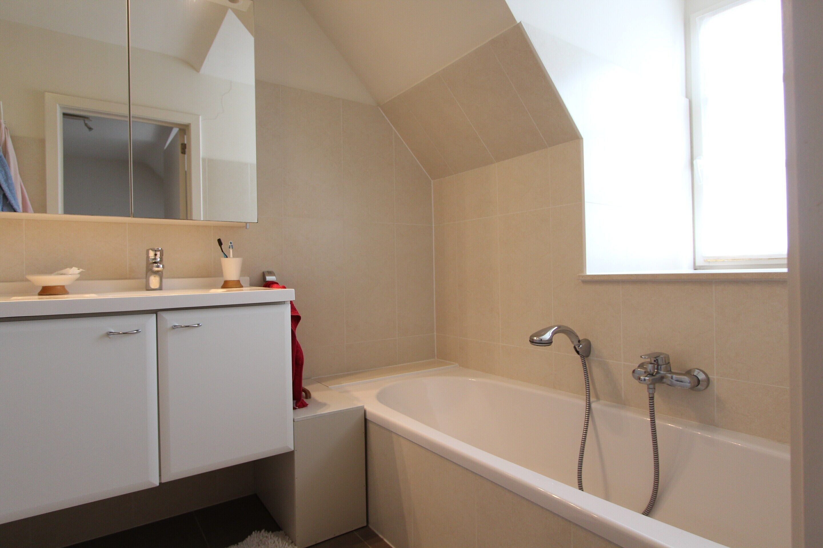 A bathroom with a bathtub, a mirror, and a window.