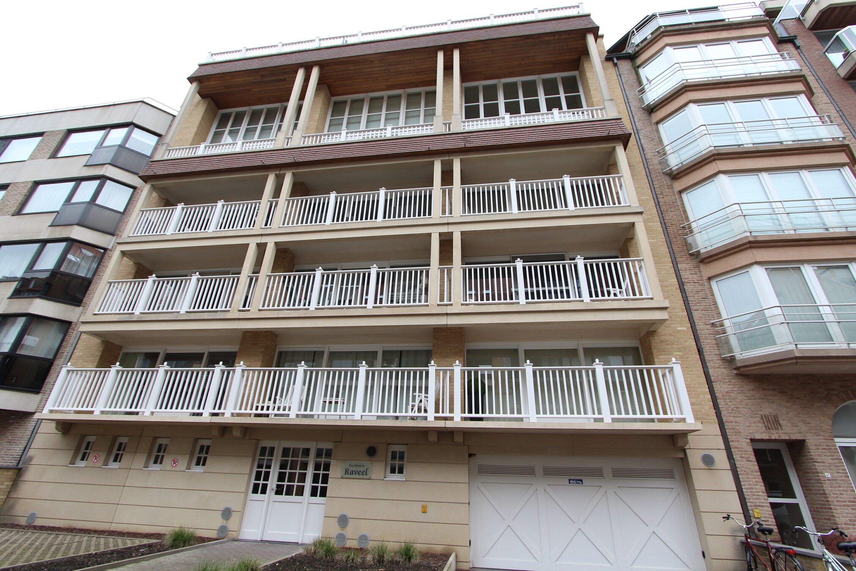 A multi-story building with balconies, a garage, and a brick facade.