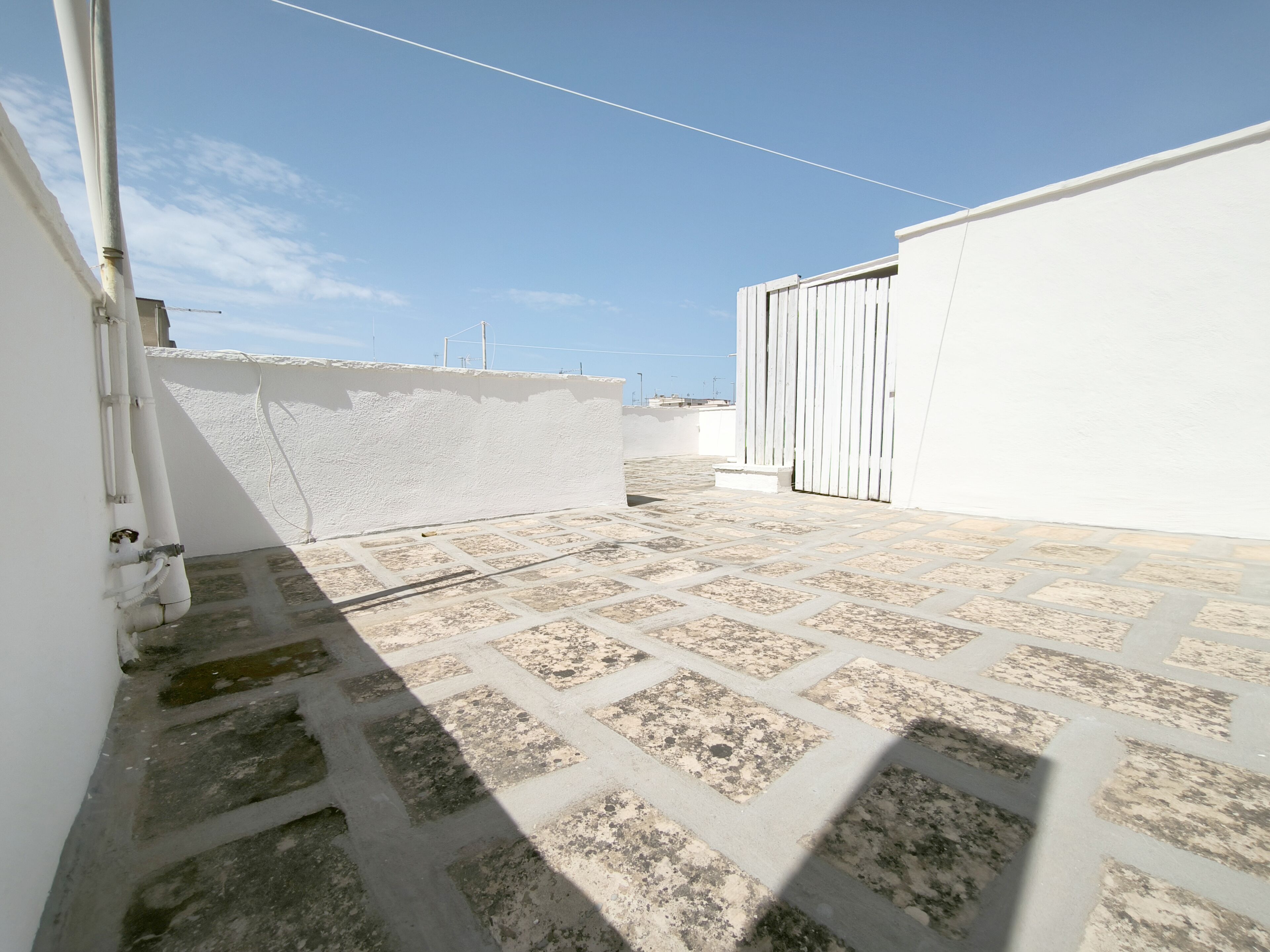 A rooftop with a tiled floor, white walls, and a metal gate.