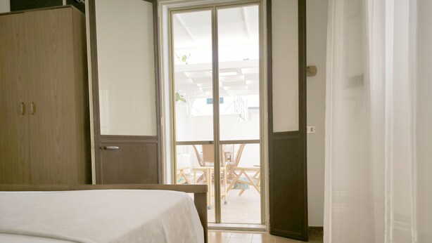 Une chambre à coucher comprenant un lit, une armoire et une porte-fenêtre coulissante donnant sur un espace extérieur avec une table et des chaises.