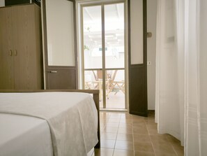Ein Schlafzimmer mit Bett, Kleiderschrank und einer Glastür, die zu einem Außenbereich mit Tisch und Stühlen führt.