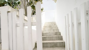 Un escalier blanc, avec un mur de pierre d’un côté et une clôture blanche de l’autre, mène à une porte située en haut.