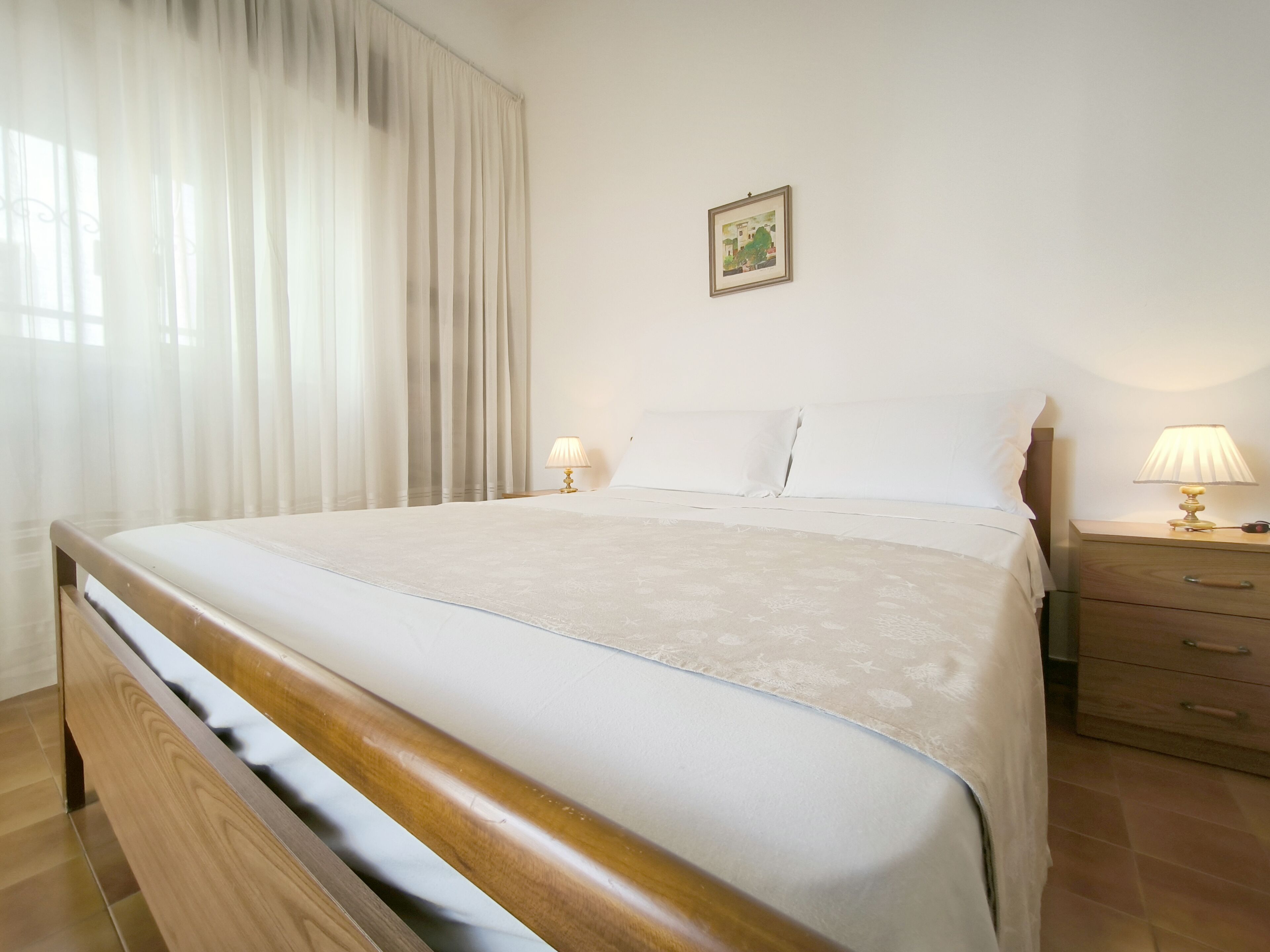 A neatly made bed with a wooden headboard, two bedside lamps, and a framed picture on the wall.
