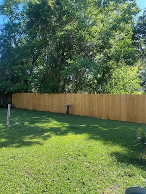 A backyard with a wooden fence, a small table, and a grassy area.