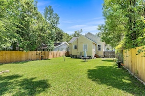 A residential backyard with a lawn, a wooden fence, and two houses. - Downtown 3BR Cottage: 5m Walk + Pets OK (Mobile)