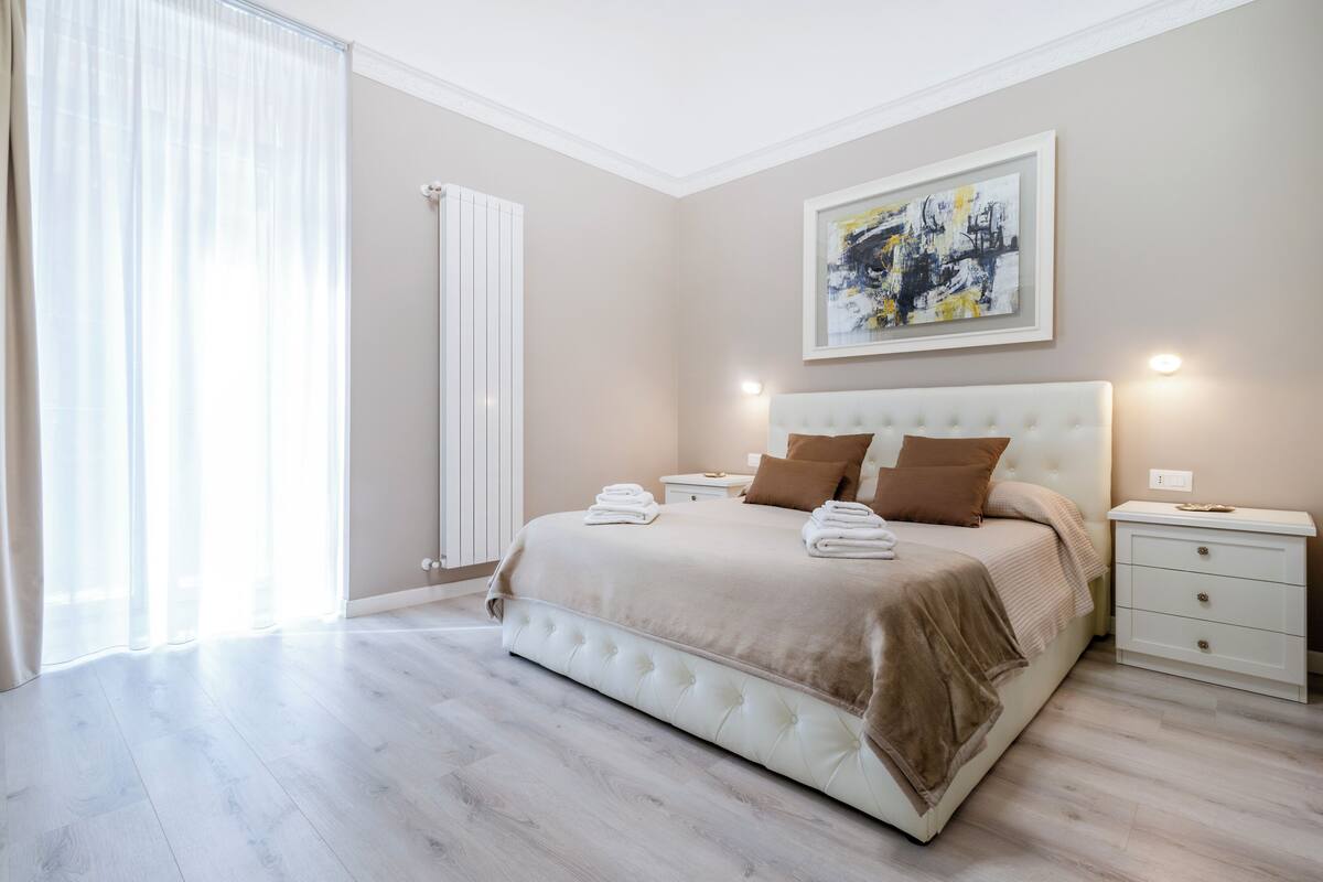 A bedroom with a large bed, bedside tables, a radiator, and a window with curtains.