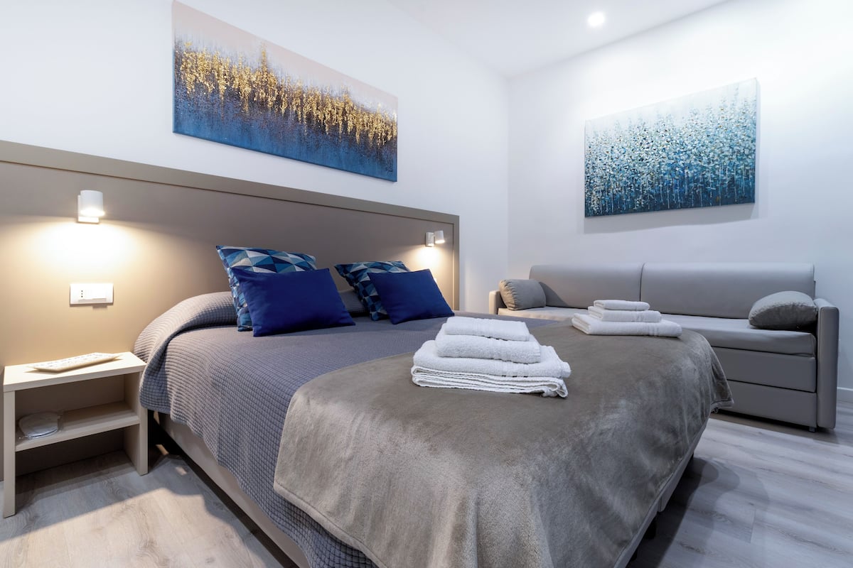 A modern bedroom with a large bed, two bedside tables, a nightstand, and a sofa.